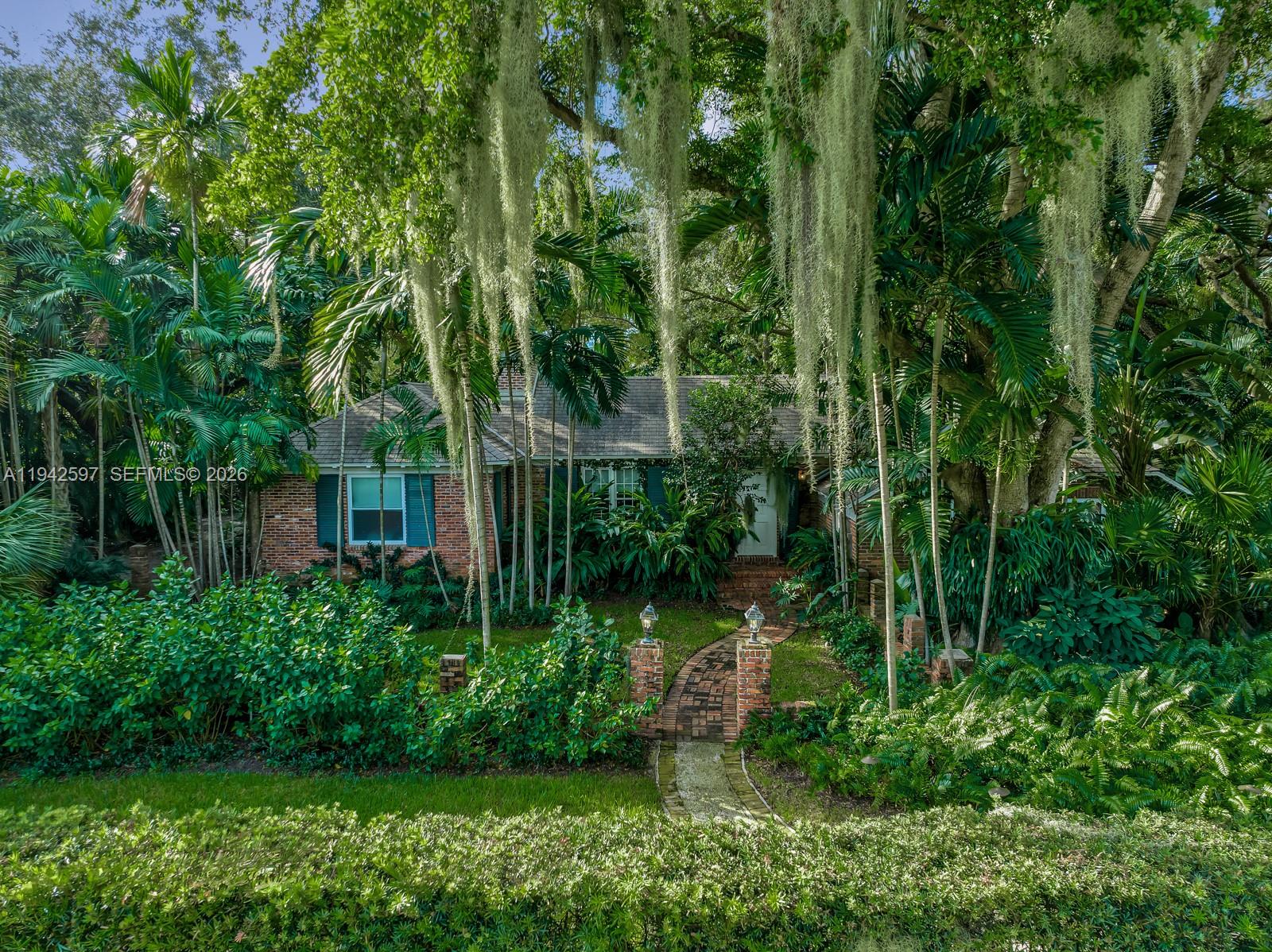 A brick house with green shutters is surrounded by lush tropical landscaping and hanging moss — 530 Melaleuca Ln, Miami FL 33137, MIAMI, FL