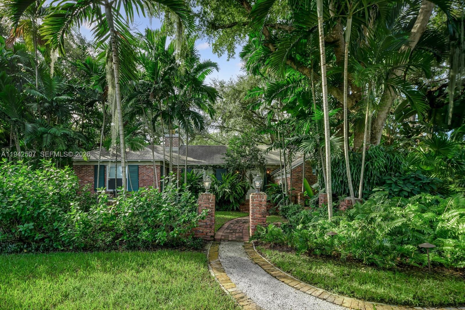 A brick house with a gravel walkway is surrounded by lush tropical trees and plants — 530 Melaleuca Ln, Miami FL 33137, MIAMI, FL