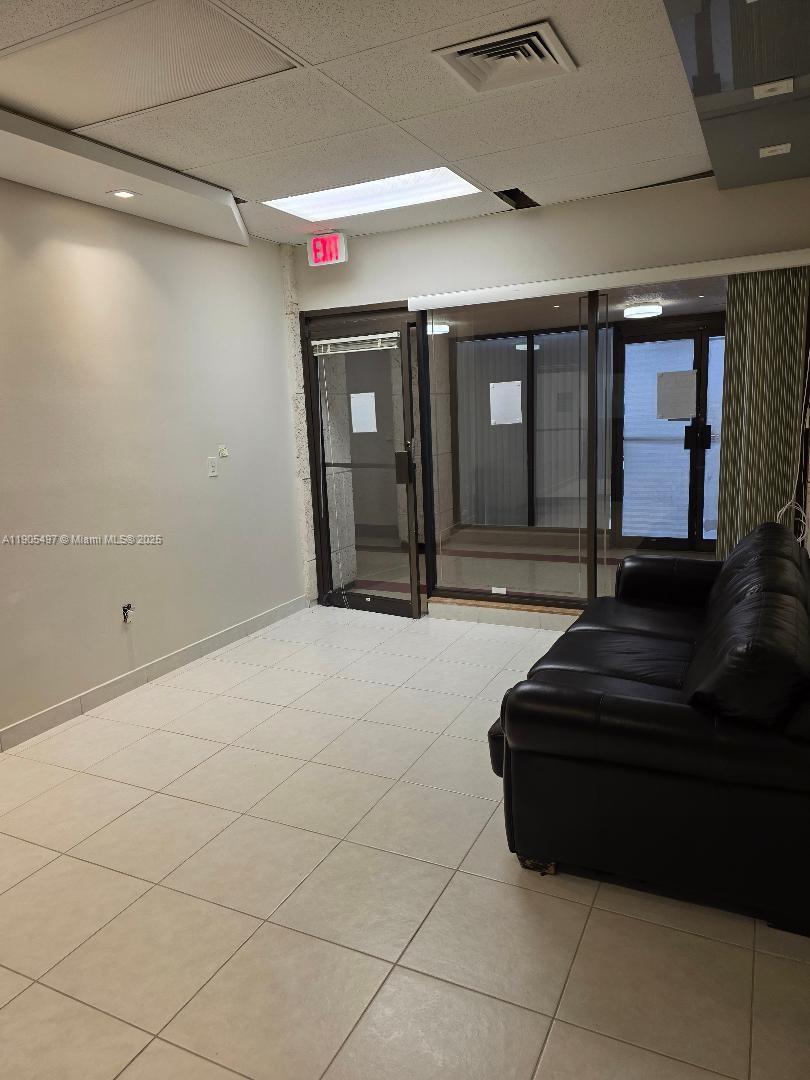 A room with light tile flooring, a black leather sofa, and a glass-paneled exit door — 1985 S Ocean Dr # 3L, Hallandale Beach FL 33009, HALLANDALE BEACH, FL
