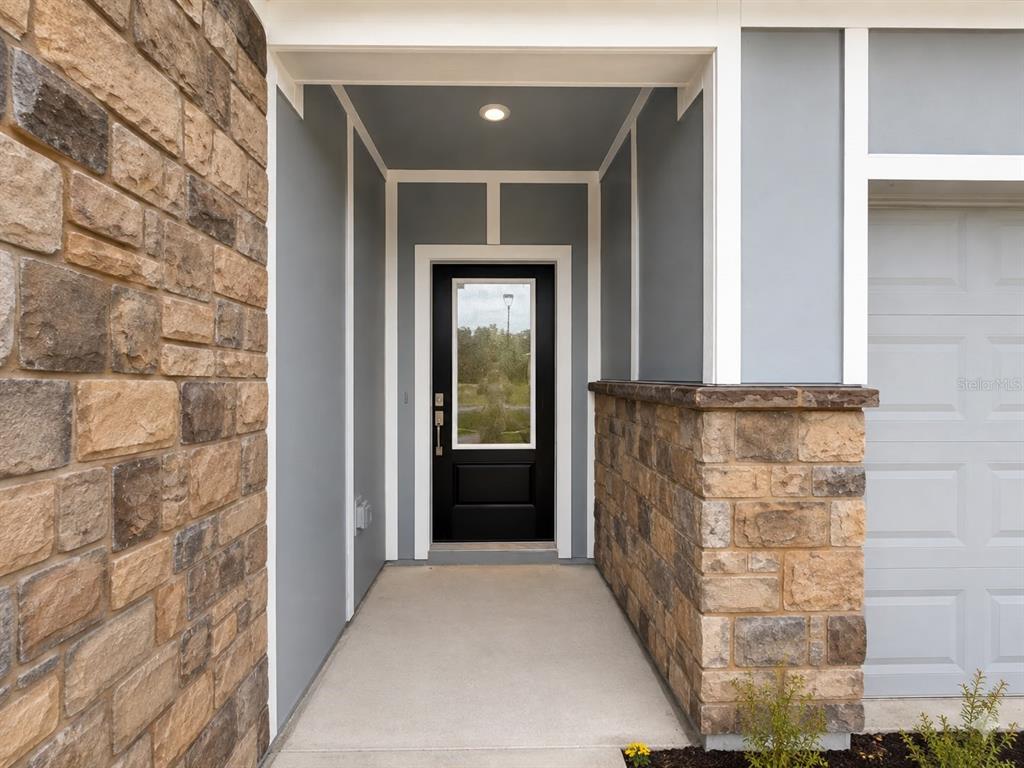 A covered entryway features a black front door, stone veneer walls, and gray siding — 817 HOUSE BOULEVARD, HAINES CITY, FL