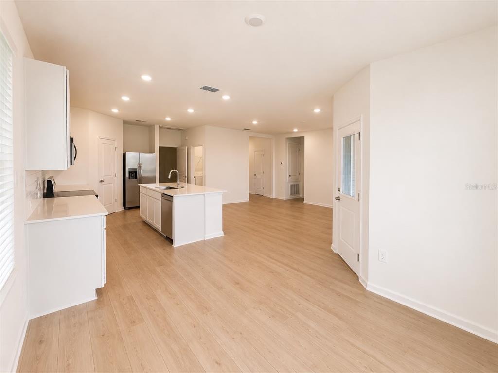 A bright, open-concept kitchen features white cabinetry, a center island, and light wood-look flooring — 817 HOUSE BOULEVARD, HAINES CITY, FL