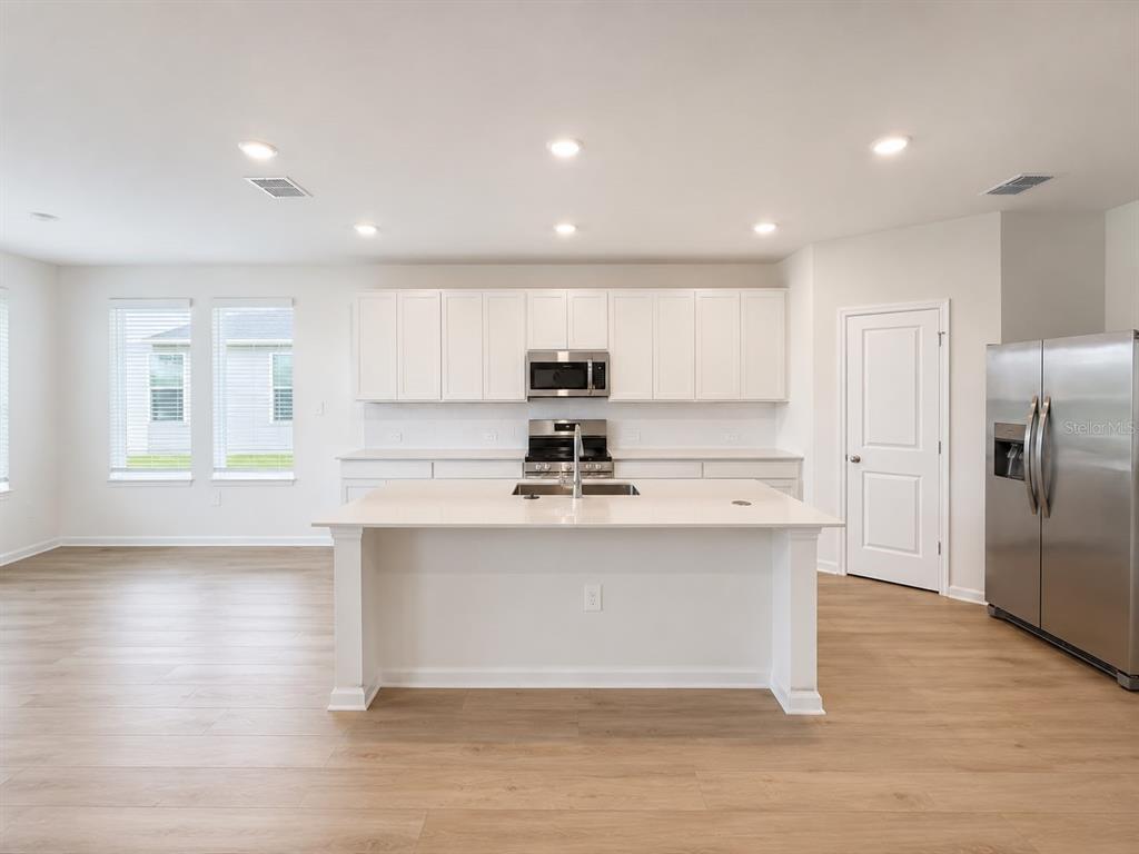 A modern kitchen features white cabinetry, a central island, stainless steel appliances, and light flooring — 817 HOUSE BOULEVARD, HAINES CITY, FL