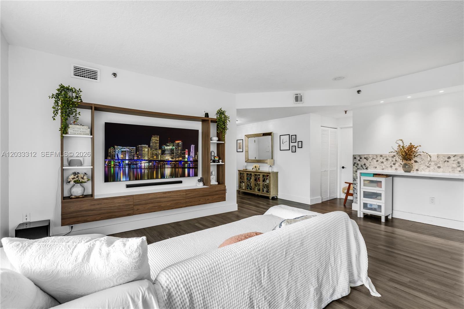 A living room features a large wall-mounted entertainment unit, white walls, and wood-look flooring — 1834 Brickell Ave # 33, Miami FL 33129, MIAMI, FL