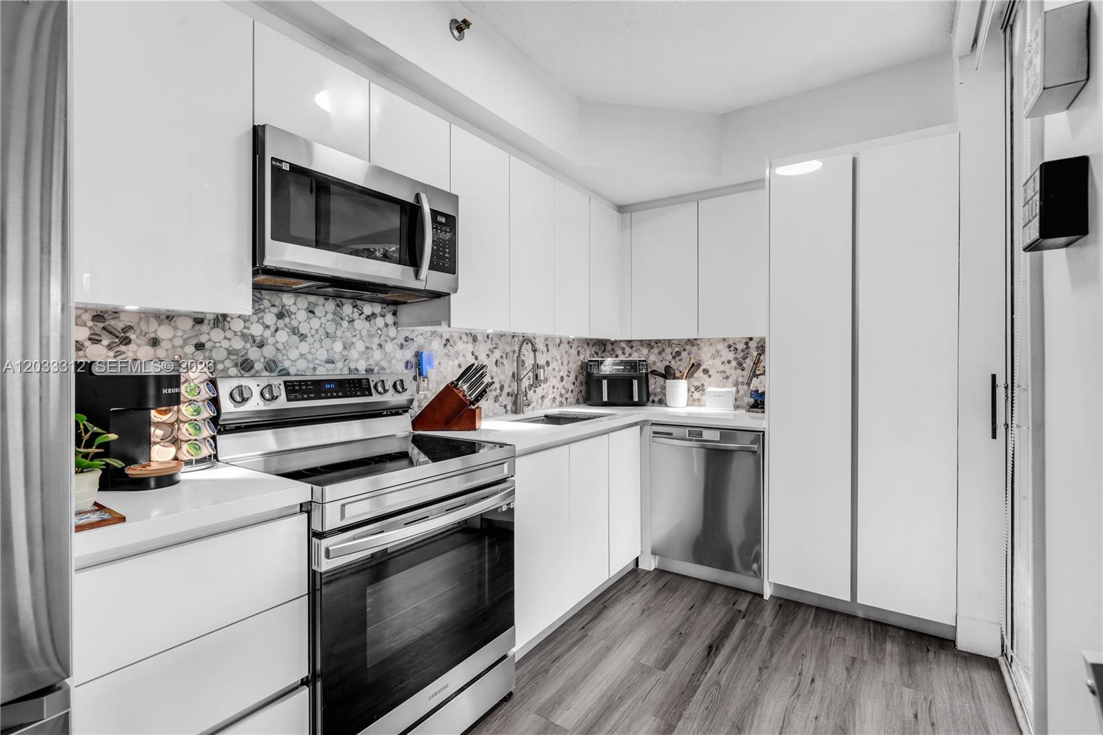 A modern kitchen features white cabinets, stainless steel appliances, and a patterned tile backsplash — 1834 Brickell Ave # 33, Miami FL 33129, MIAMI, FL