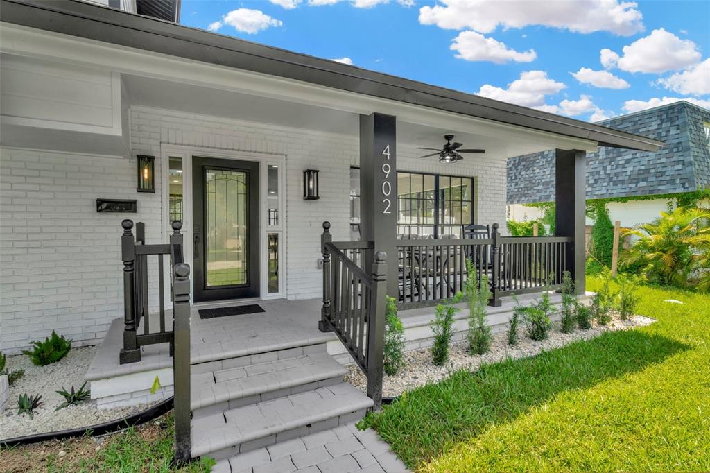 A white brick house features a covered front porch with black railings and a door — 4902 W SAN RAFAEL STREET, TAMPA, FL