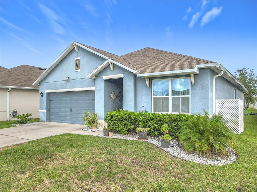 A blue single-story house with a two-car garage, a shingled roof, and front landscaping — 1765 BROCKRIDGE ROAD, KISSIMMEE, FL