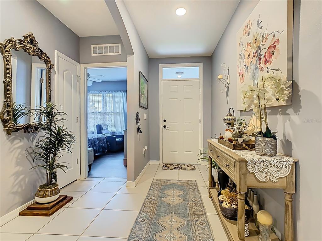 A bright entryway features tile flooring, a console table, a decorative mirror, and a rug — 1765 BROCKRIDGE ROAD, KISSIMMEE, FL