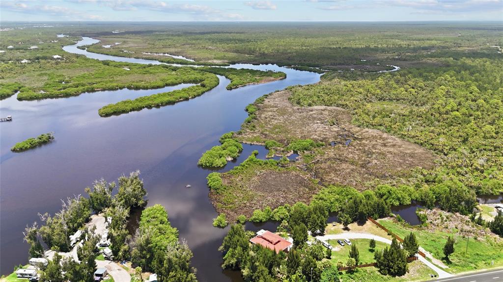 An aerial view shows a river winding through a marshy landscape with nearby residential properties — 10007 TAMIAMI TRAIL S, NORTH PORT, FL