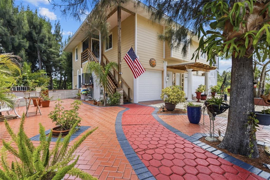 A two-story house with yellow siding, a red brick patio, and a red paved walkway — 10007 TAMIAMI TRAIL S, NORTH PORT, FL