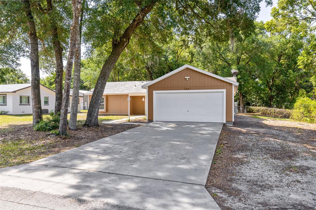 A brown house with a white garage door and a concrete driveway under large trees — 45 LAKE DRIVE, DEBARY, FL