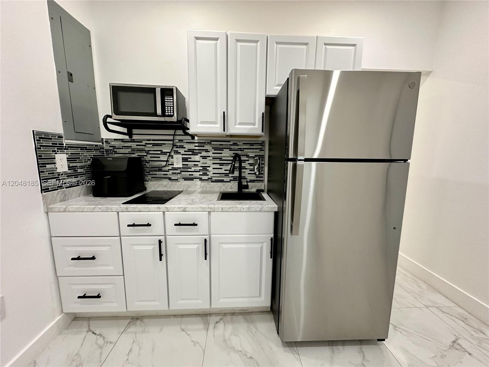 A small kitchen features white cabinets, stainless steel appliances, and a black-and-white tiled backsplash — 1309 NW 55th Ter, Miami FL 33142, MIAMI, FL