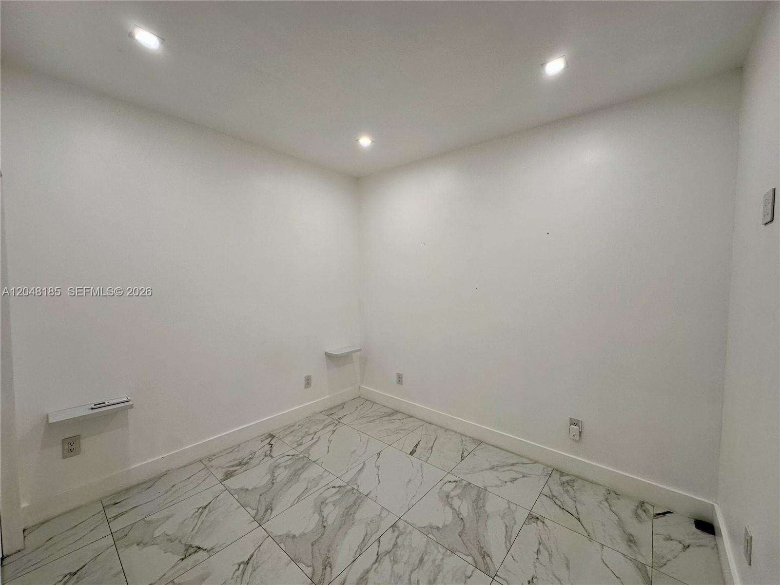 A small, empty room features white walls, recessed ceiling lights, and white marble-patterned tile flooring — 1309 NW 55th Ter, Miami FL 33142, MIAMI, FL