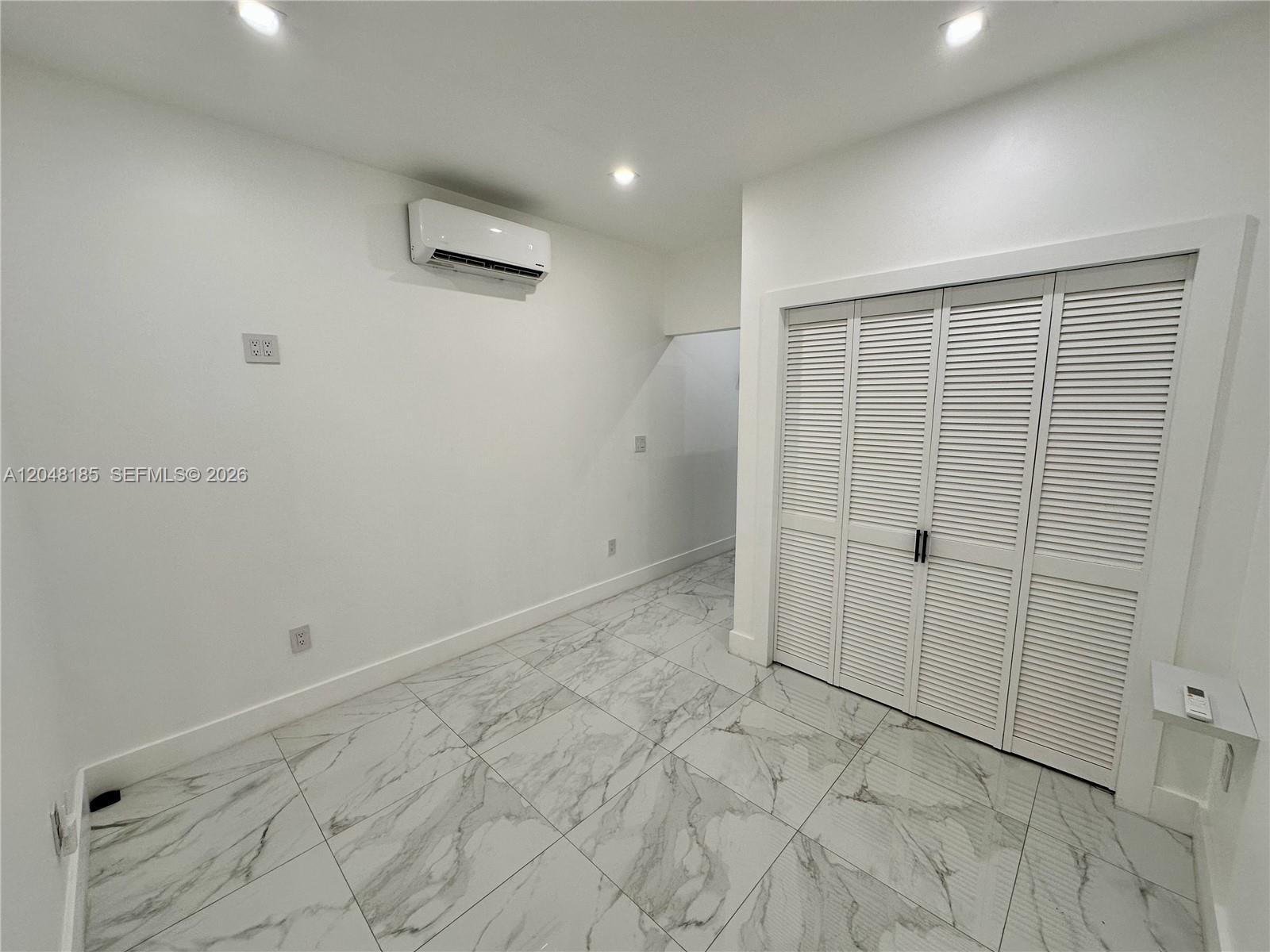 A room with white walls, marble-patterned tile flooring, a wall-mounted air conditioner, and louvered closet doors — 1309 NW 55th Ter, Miami FL 33142, MIAMI, FL