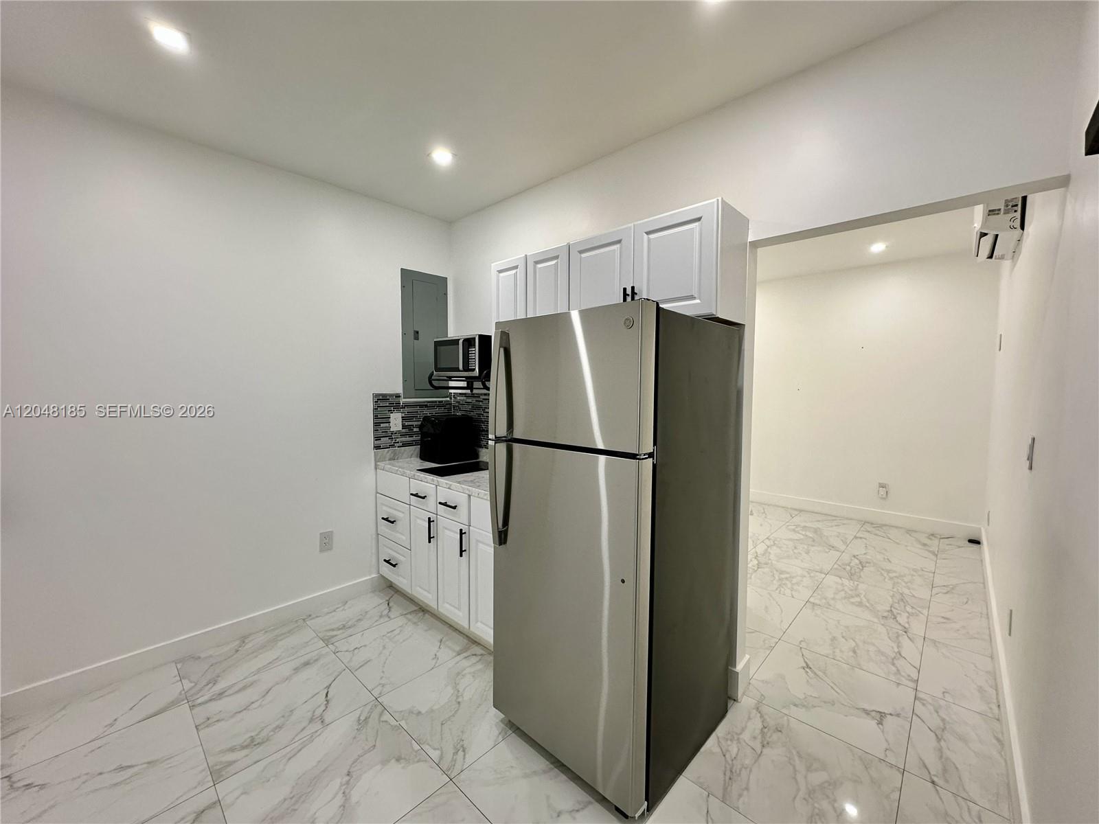 A small kitchen features white cabinets, stainless steel appliances, and white marble-patterned tile flooring — 1309 NW 55th Ter, Miami FL 33142, MIAMI, FL