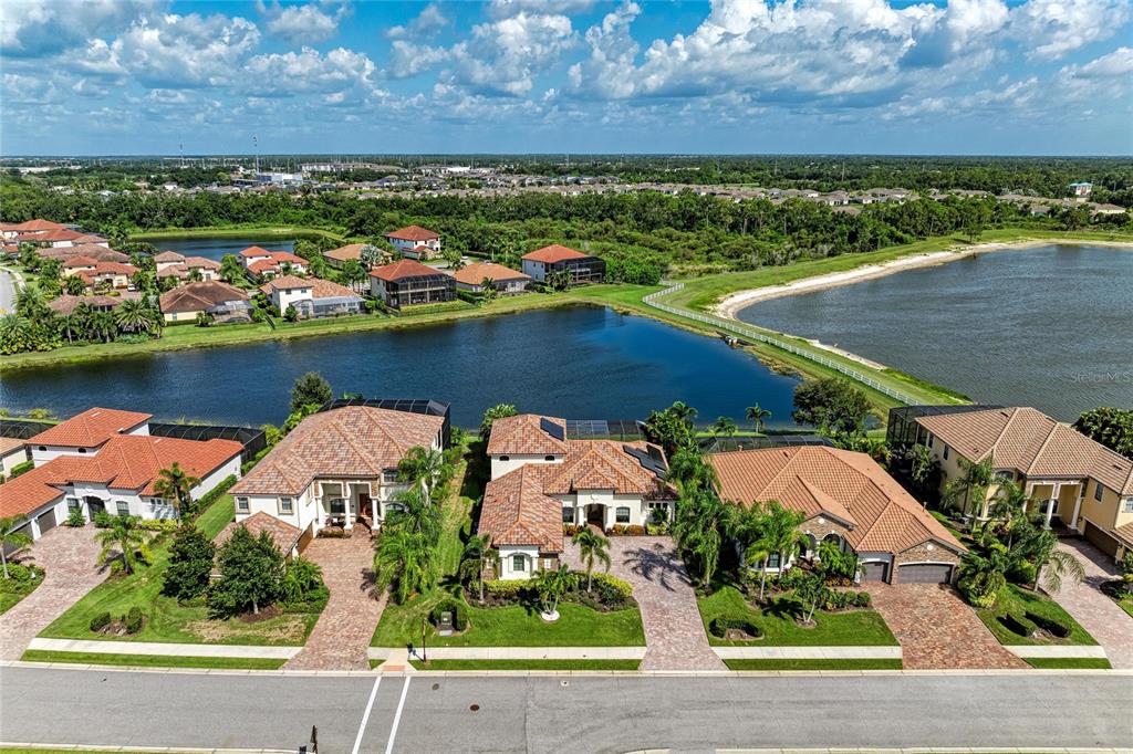 An aerial view shows several suburban houses with tile roofs situated along a large lake — 5664 CLOVERLEAF RUN, LAKEWOOD RANCH, FL