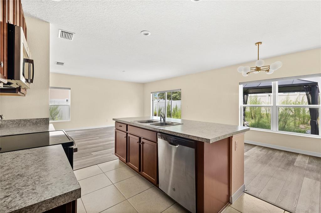 A kitchen with a center island, stainless steel dishwasher, and tile flooring overlooks a living area — 922 ANNA PLACE, DAVENPORT, FL