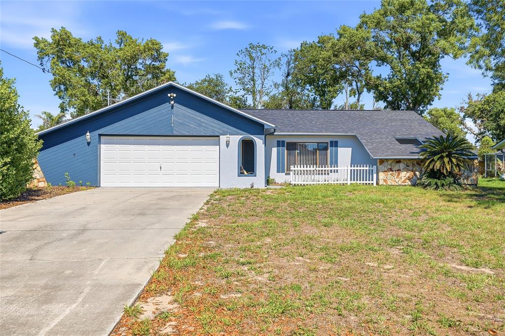 A single-story house features a blue-painted garage, a stone facade, and a white picket fence — 3276 MORVEN DRIVE, SPRING HILL, FL