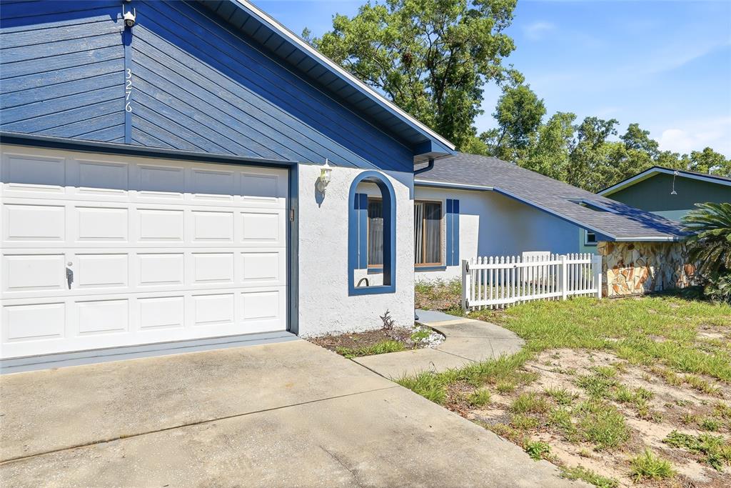 A blue and white house exterior features a garage, a white fence, and stone accents — 3276 MORVEN DRIVE, SPRING HILL, FL