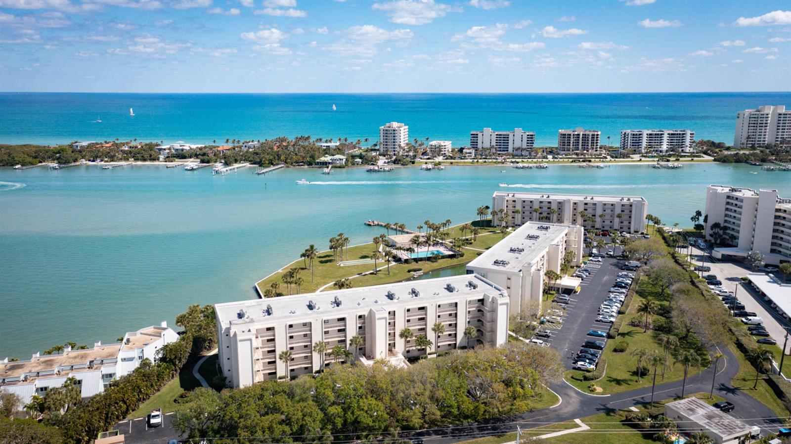 An aerial view shows multi-story apartment buildings situated along a waterfront with a parking lot — 300 Intracoastal Place # 403, Jupiter FL 33469, JUPITER, FL
