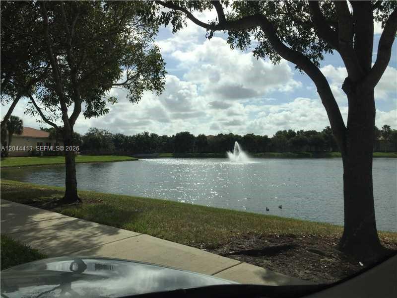 A view of a lake with a fountain, framed by trees and a sidewalk — 2464 Centergate Dr # 101, Miramar FL 33025, MIRAMAR, FL