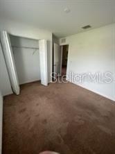 A bedroom features brown carpeting, white walls, and an open closet with bifold doors — 6 WOOD AMBER LANE UNIT A, PALM COAST, FL