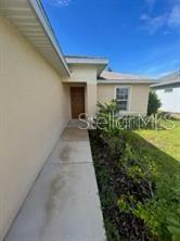 A concrete walkway leads to the front entrance of a beige house with a wooden door — 6 WOOD AMBER LANE UNIT A, PALM COAST, FL