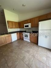 A kitchen features wood cabinets, white appliances, dark countertops, and light-colored tile flooring — 6 WOOD AMBER LANE UNIT A, PALM COAST, FL