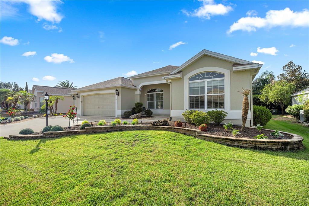 A single-story house with a beige stucco exterior, a two-car garage, and a curved stone planter — 346 PACOLET TERRACE, THE VILLAGES, FL