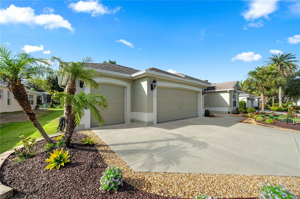 A beige house with a three-car garage and a landscaped front yard under a blue sky — 346 PACOLET TERRACE, THE VILLAGES, FL