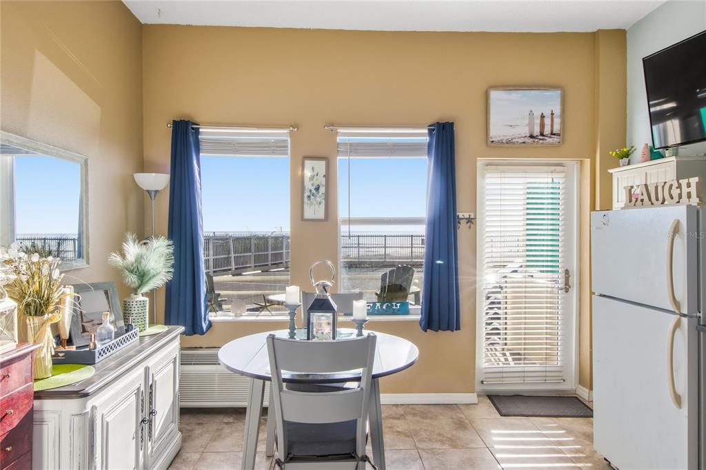 A dining area features a round table, two windows with blue curtains, and a refrigerator — 701 S ATLANTIC AVENUE UNIT 112, DAYTONA BEACH, FL