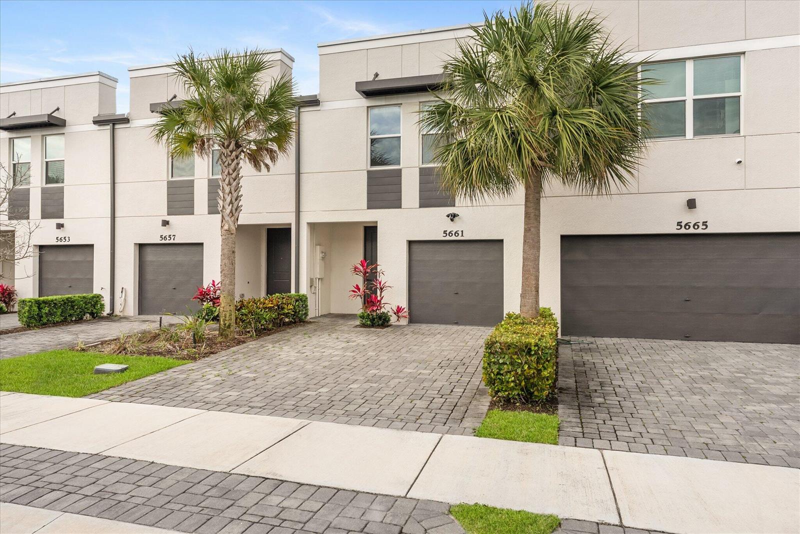 A row of modern townhouses features gray garage doors, paved driveways, and palm trees — 5661 Mentmore Drive, Mangonia Park FL 33407, MANGONIA PARK, FL