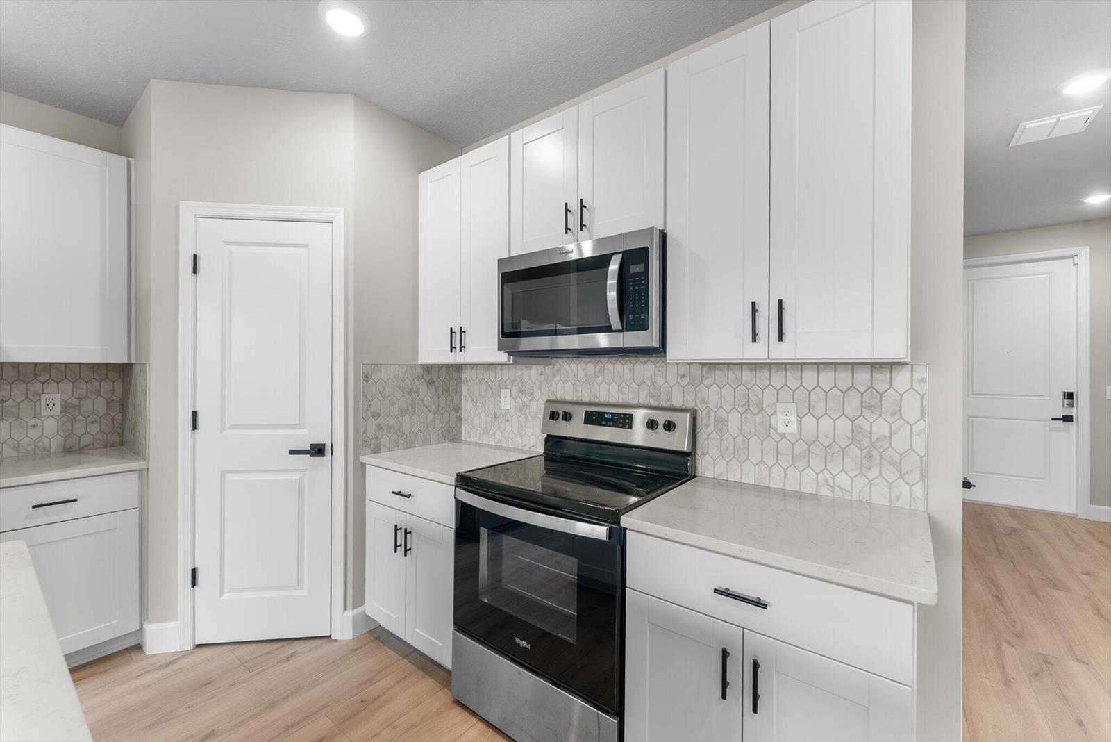 A kitchen features white cabinets, stainless steel appliances, and a light-colored hexagonal tile backsplash — 5661 Mentmore Drive, Mangonia Park FL 33407, MANGONIA PARK, FL