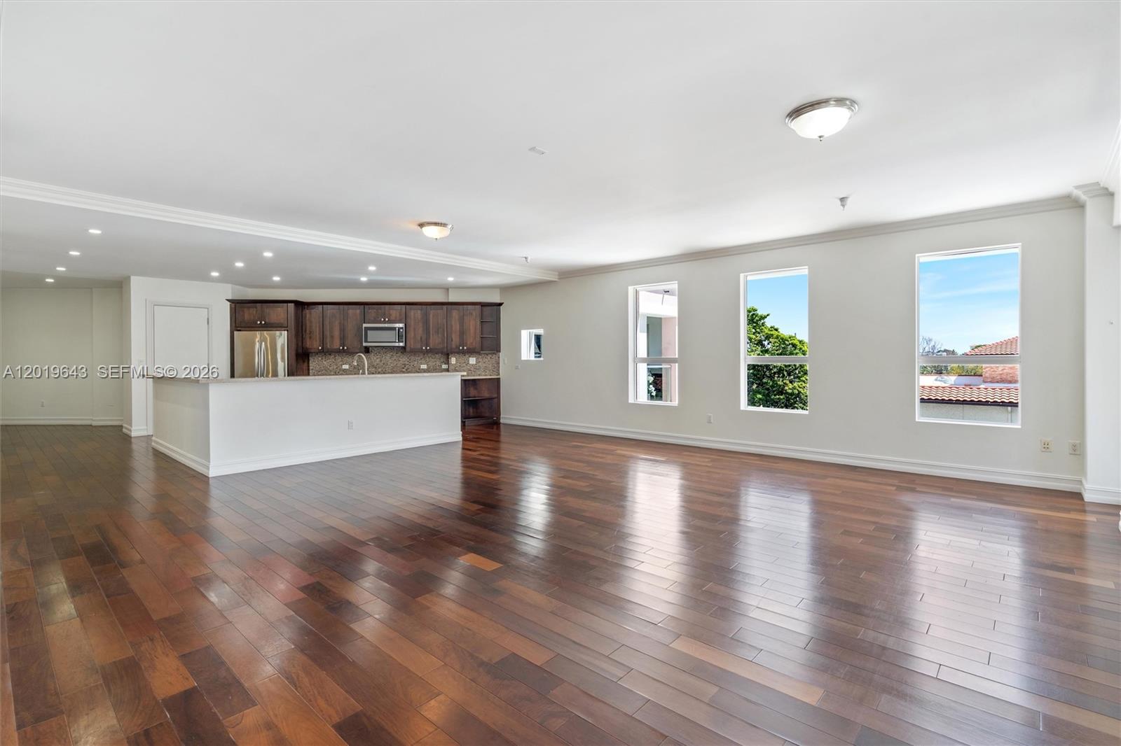 An open-concept living area features dark hardwood floors, a kitchen with wooden cabinets, and windows — 455 E Palmetto Park Rd # 3, Boca Raton FL 33432, BOCA RATON, FL