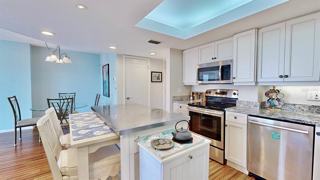 A kitchen features white cabinets, stainless steel appliances, a metal-topped island, and an adjacent dining area — 4900 BRITTANY DRIVE S UNIT 1011, ST PETERSBURG, FL