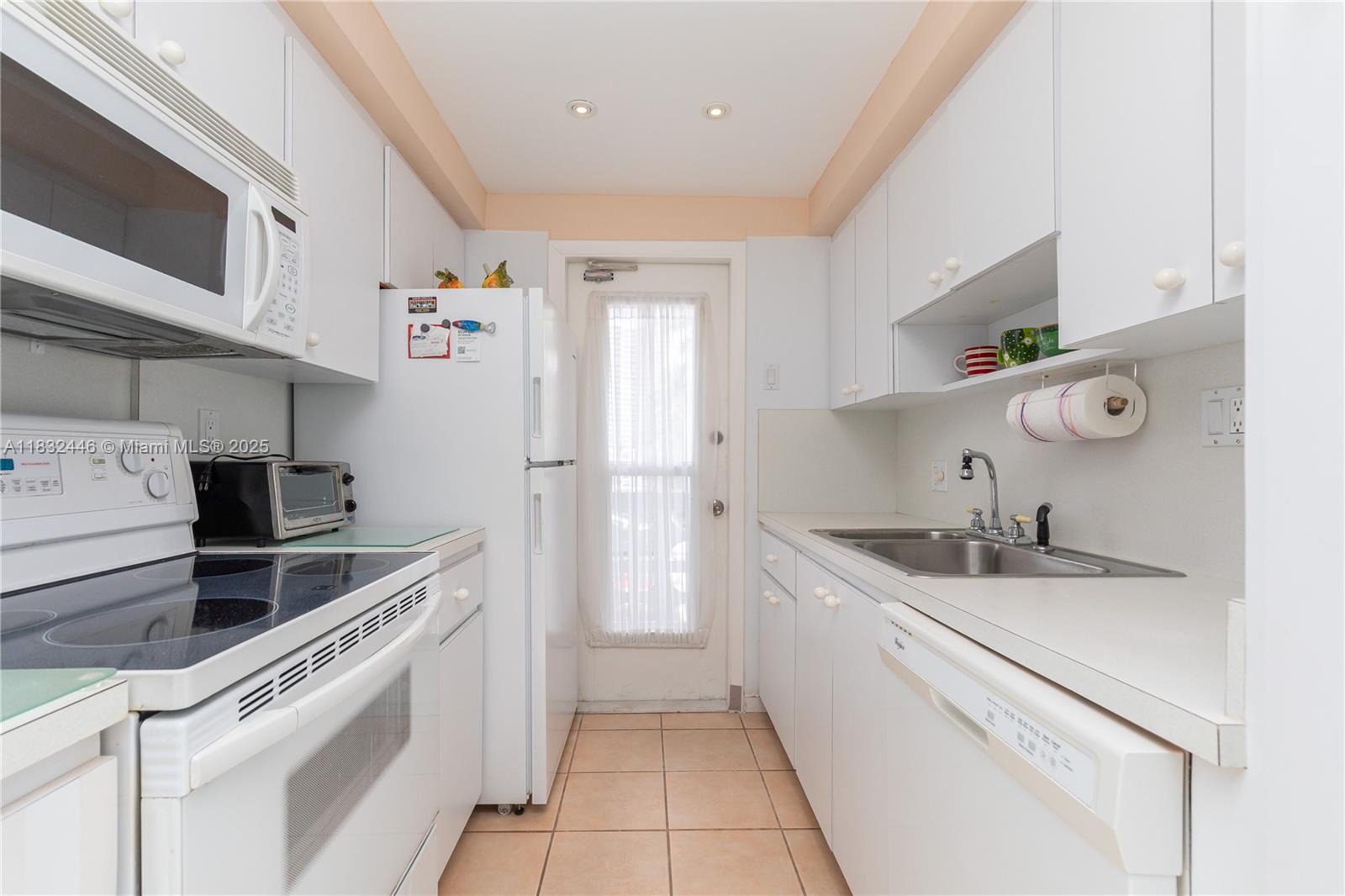 A galley kitchen features white cabinetry, white appliances, a stainless steel sink, and tiled flooring — 3135 S Ocean Dr # 230, Hallandale Beach FL 33009, HALLANDALE BEACH, FL