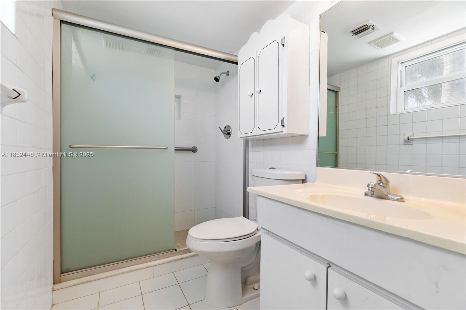 A white bathroom features a glass-enclosed shower, a toilet, and a vanity with a mirror — 3135 S Ocean Dr # 230, Hallandale Beach FL 33009, HALLANDALE BEACH, FL