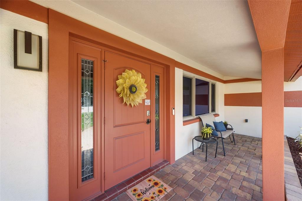 A front porch features a terracotta-colored door with a sunflower wreath and a paver floor — 5915 46TH AVENUE N, KENNETH CITY, FL