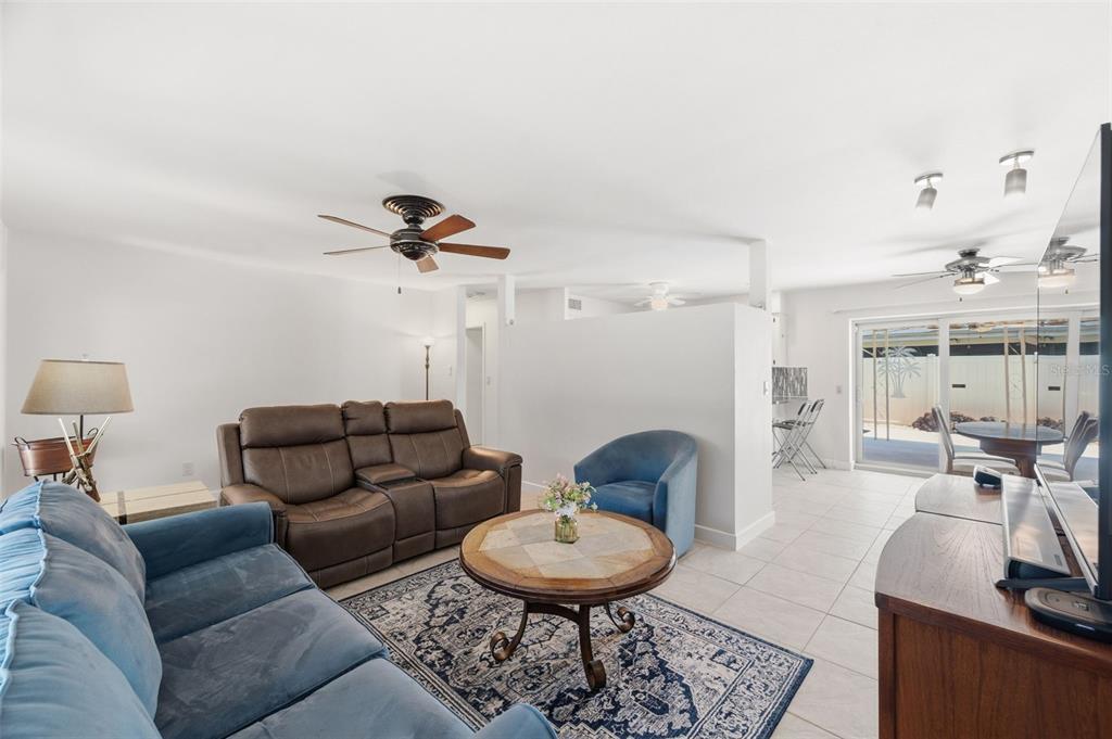 A living room features a blue sofa, brown loveseat, tile flooring, and a sliding glass door — 5915 46TH AVENUE N, KENNETH CITY, FL