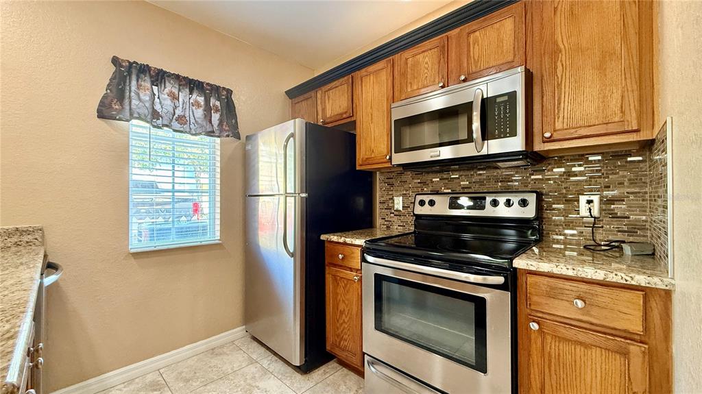 A kitchen features wood cabinets, stainless steel appliances, granite countertops, and a tiled backsplash — 4005 SAN SEBASTIAN DRIVE UNIT 107, KISSIMMEE, FL