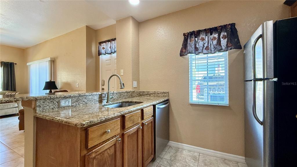 A kitchen features granite countertops, wood cabinets, a stainless steel dishwasher, and a window — 4005 SAN SEBASTIAN DRIVE UNIT 107, KISSIMMEE, FL