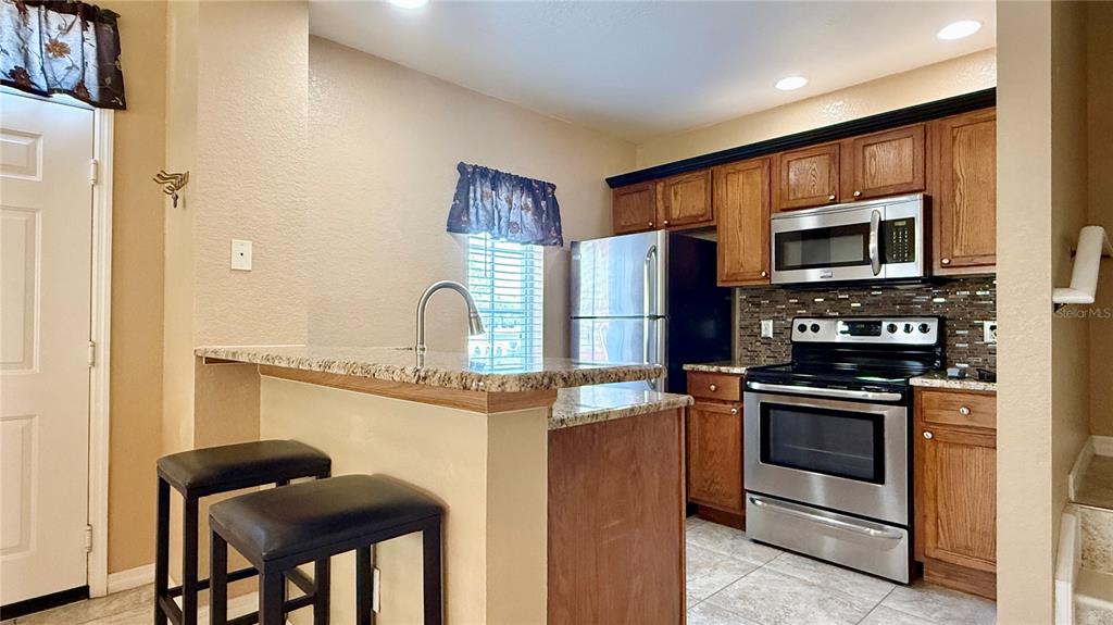 A kitchen features wood cabinets, stainless steel appliances, a granite breakfast bar, and tile flooring — 4005 SAN SEBASTIAN DRIVE UNIT 107, KISSIMMEE, FL