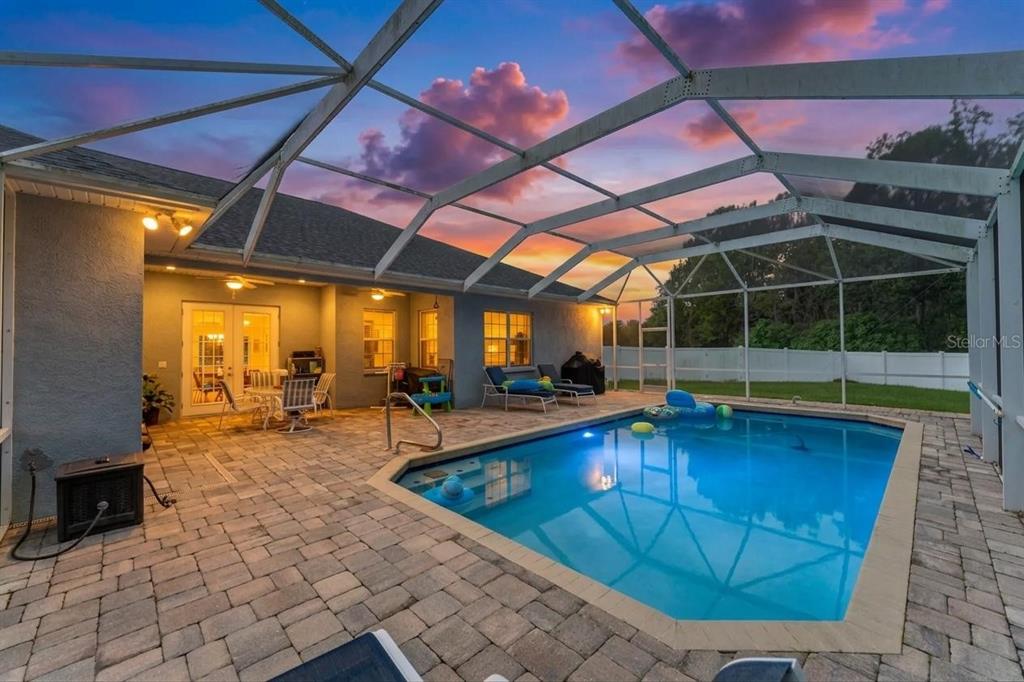 A backyard swimming pool with a screened enclosure and paved patio at sunset — 1318 LITTLE ALAFIA DRIVE, PLANT CITY, FL