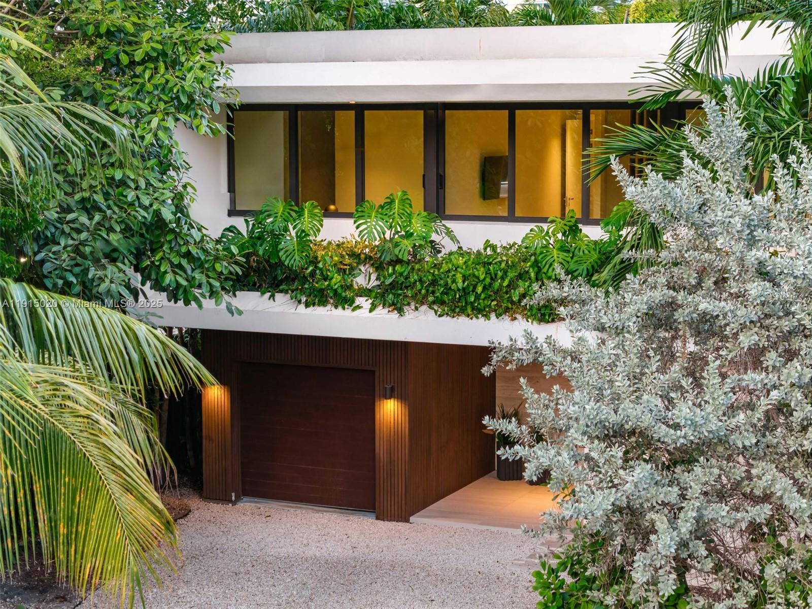 A modern two-story house features a wood-paneled garage, large windows, and lush exterior landscaping — 77 SW 18th Terrace, Miami FL 33129, MIAMI, FL