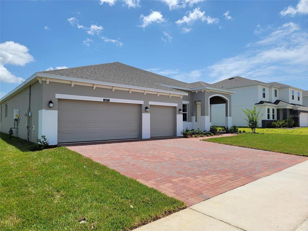 A single-story house with a three-car garage and a paved driveway under a blue sky — 5073 NORTHERN DOVE AVENUE, MOUNT DORA, FL