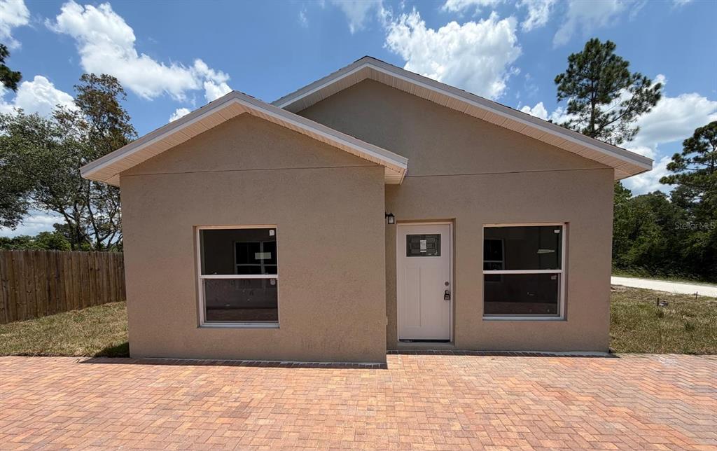 A single-story house with a tan stucco exterior, a white front door, and a paver driveway — 1214 7TH AVENUE, DELAND, FL