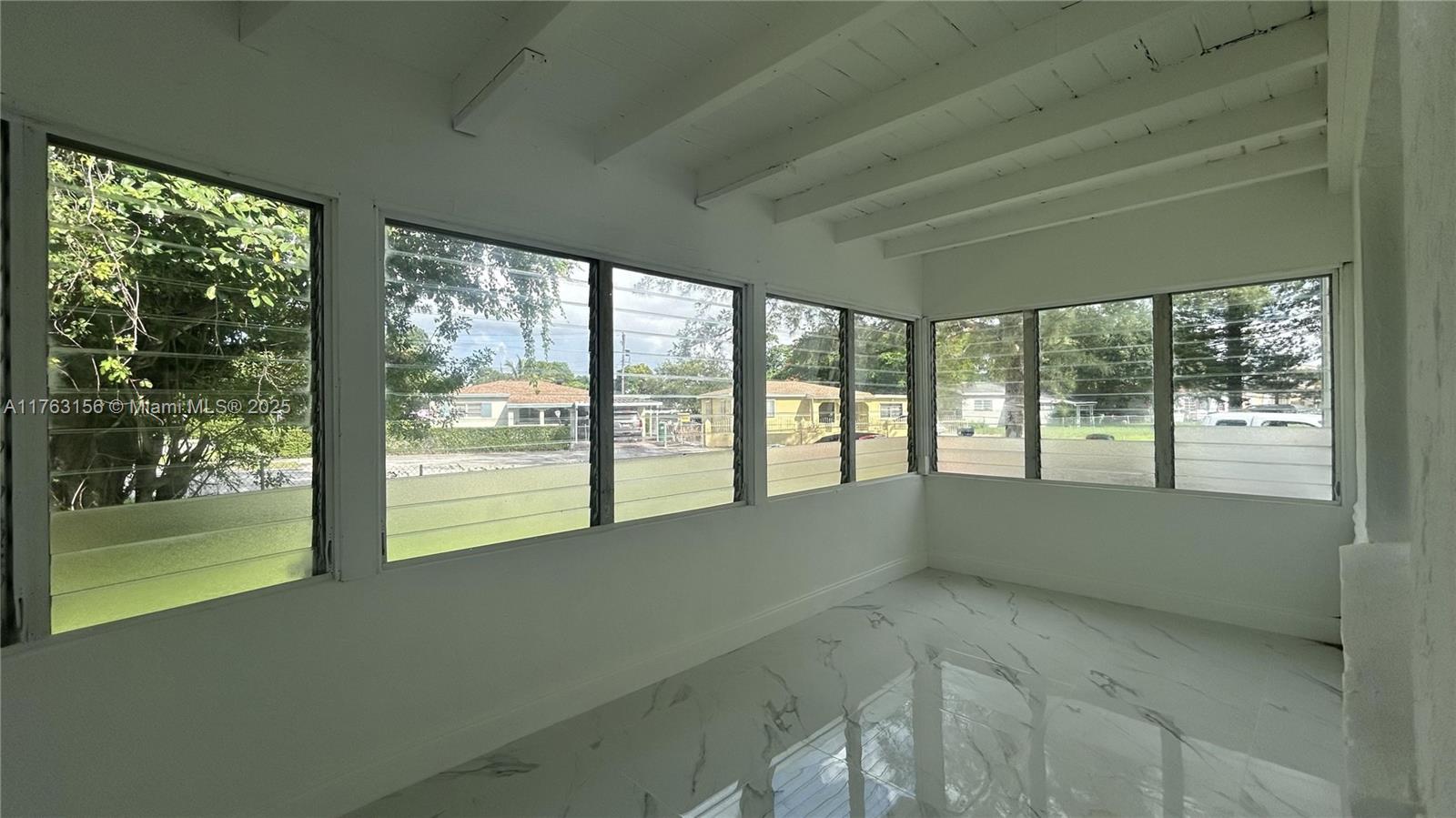 A sunroom features white marble-look tile flooring, exposed ceiling beams, and multiple louvered glass windows — 205 Seaman Ave, Opa-Locka FL 33054, OPA-LOCKA, FL