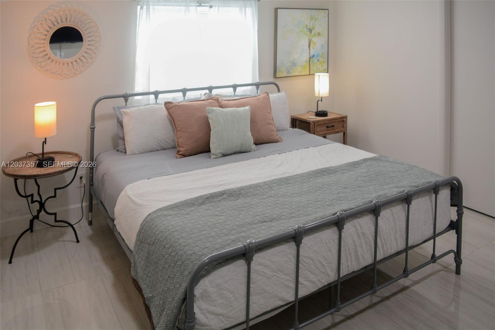 A bedroom features a gray metal bed frame, two bedside tables, and a round wall mirror — FORT LAUDERDALE, FL