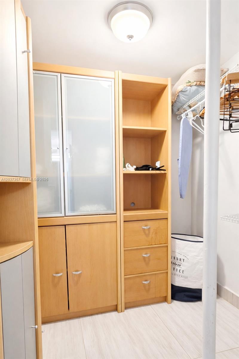 A closet features light wood cabinetry with glass-front doors, open shelving, drawers, and a laundry hamper — FORT LAUDERDALE, FL