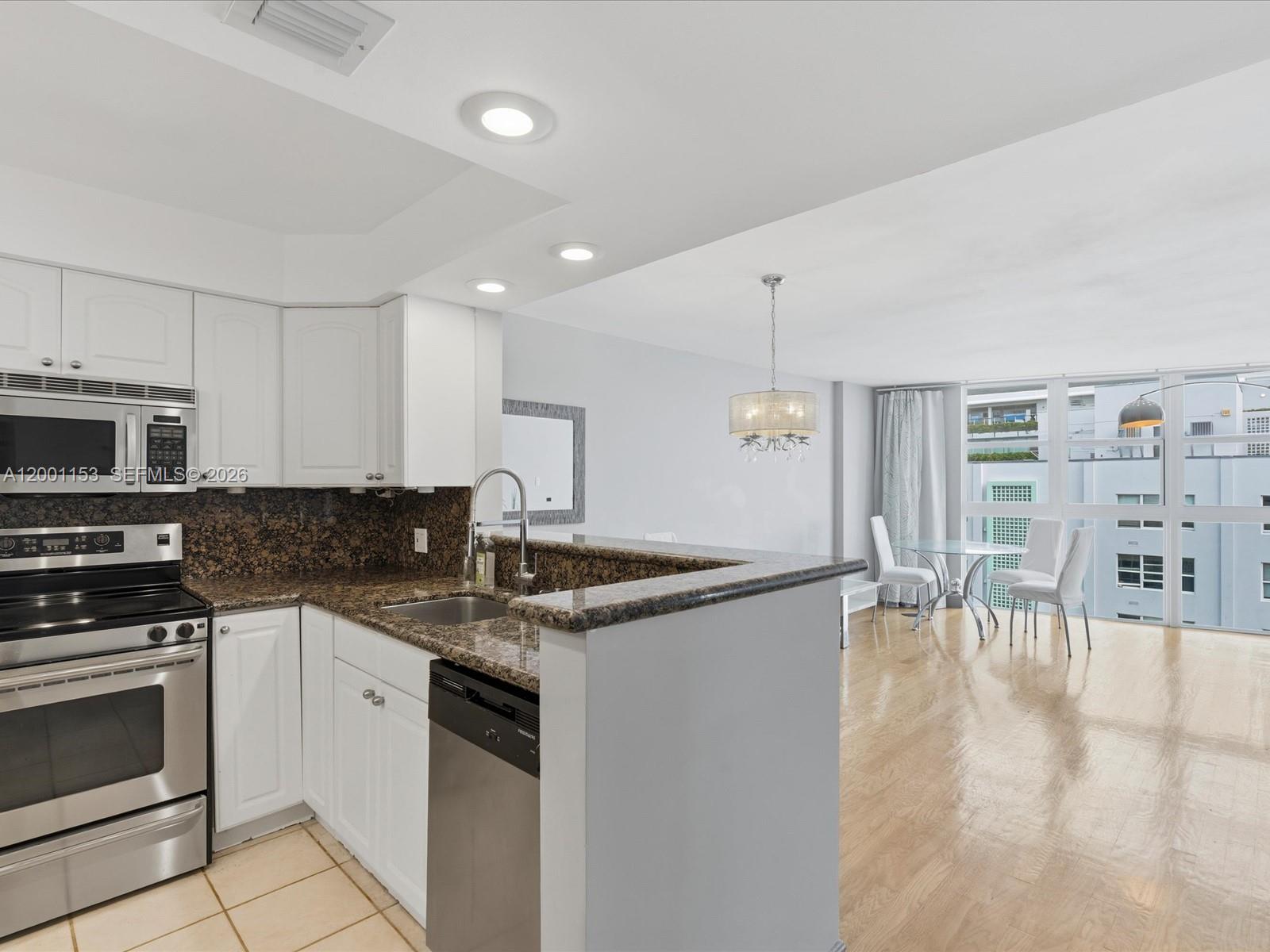 A kitchen with white cabinets and granite countertops overlooks a dining area with floor-to-ceiling windows — 1228 West Ave # 1506, Miami Beach FL 33139, MIAMI BEACH, FL