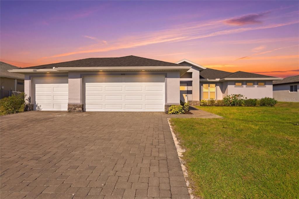 A single-story house with a three-car garage and a paved driveway at sunset — 3600 NE 20TH PLACE, CAPE CORAL, FL